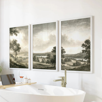 Three-piece trees and fields wall art in white frames, displayed above a freestanding soaking tub in a bathroom.