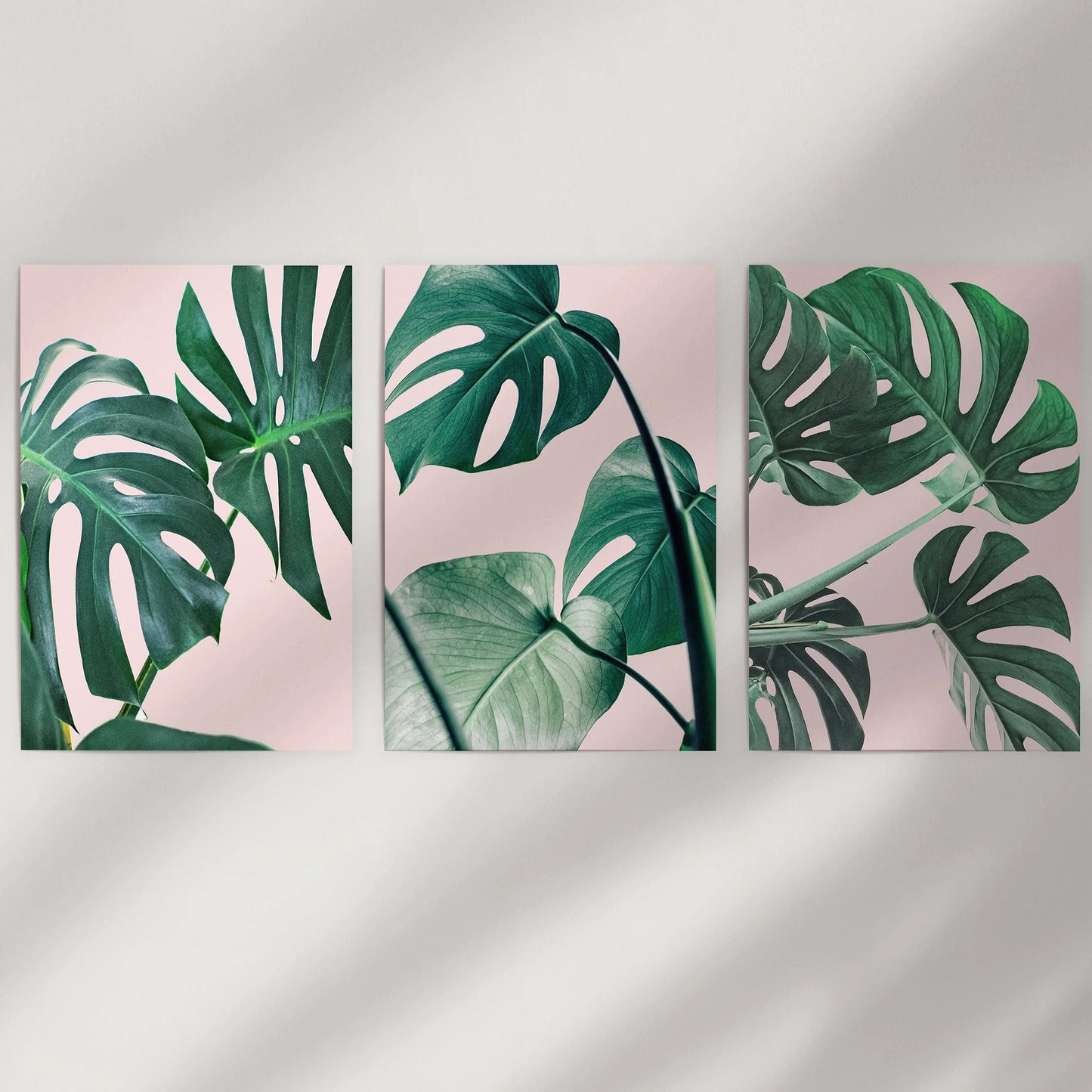 Unframed pink tropical plant prints form a minimalist three-piece wall display above the bed, blending blush hues with fresh green notes.