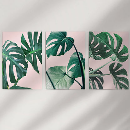 Unframed pink tropical plant prints form a minimalist three-piece wall display above the bed, blending blush hues with fresh green notes.
