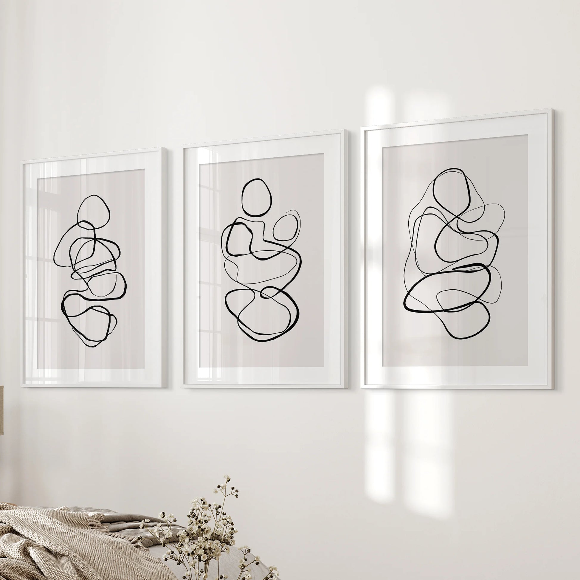 A 3-print gallery wall of abstract line drawings, matted and white-framed, aligns neatly beside the bedroom bed for a polished finish.