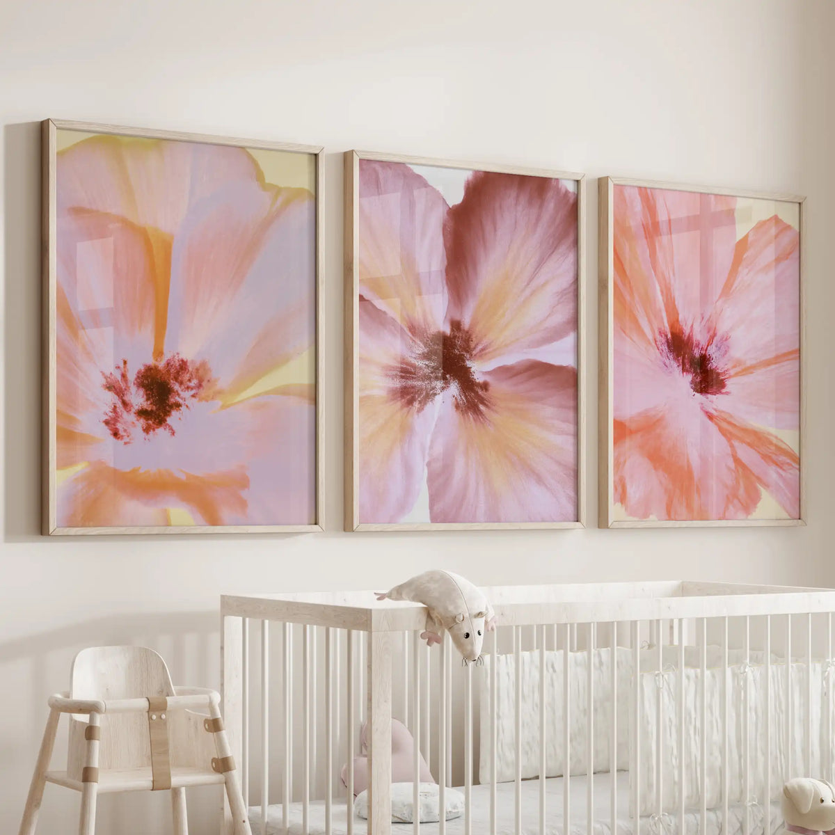 Three pastel flower close-up prints hang above a nursery crib, framed in oak.