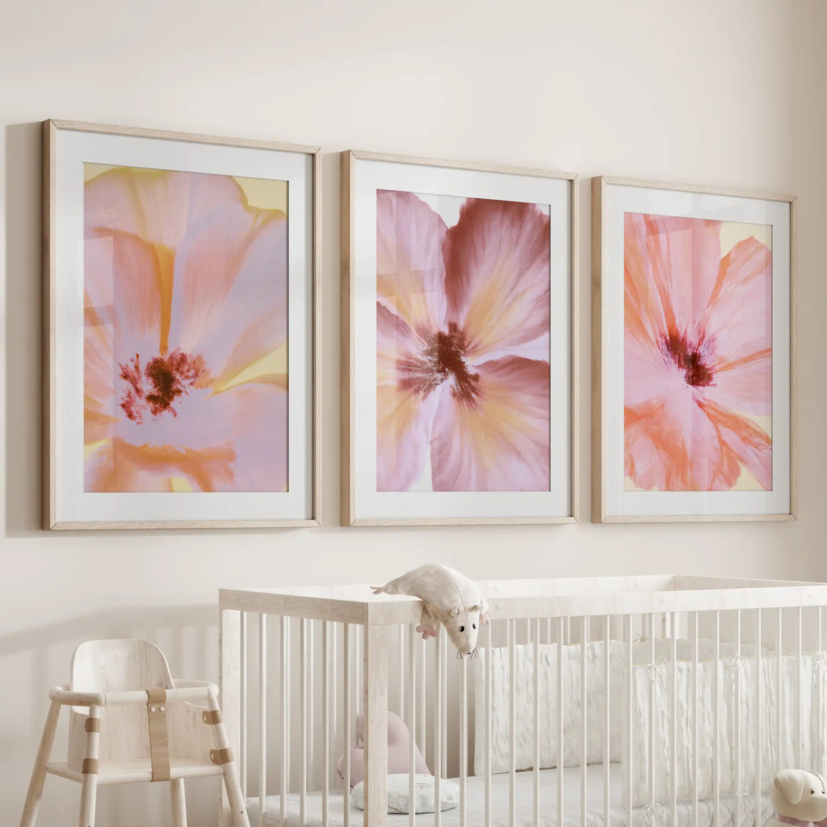 The three oak frames above a crib have white mats around flower close-ups in pink and peach, with dark red centers.