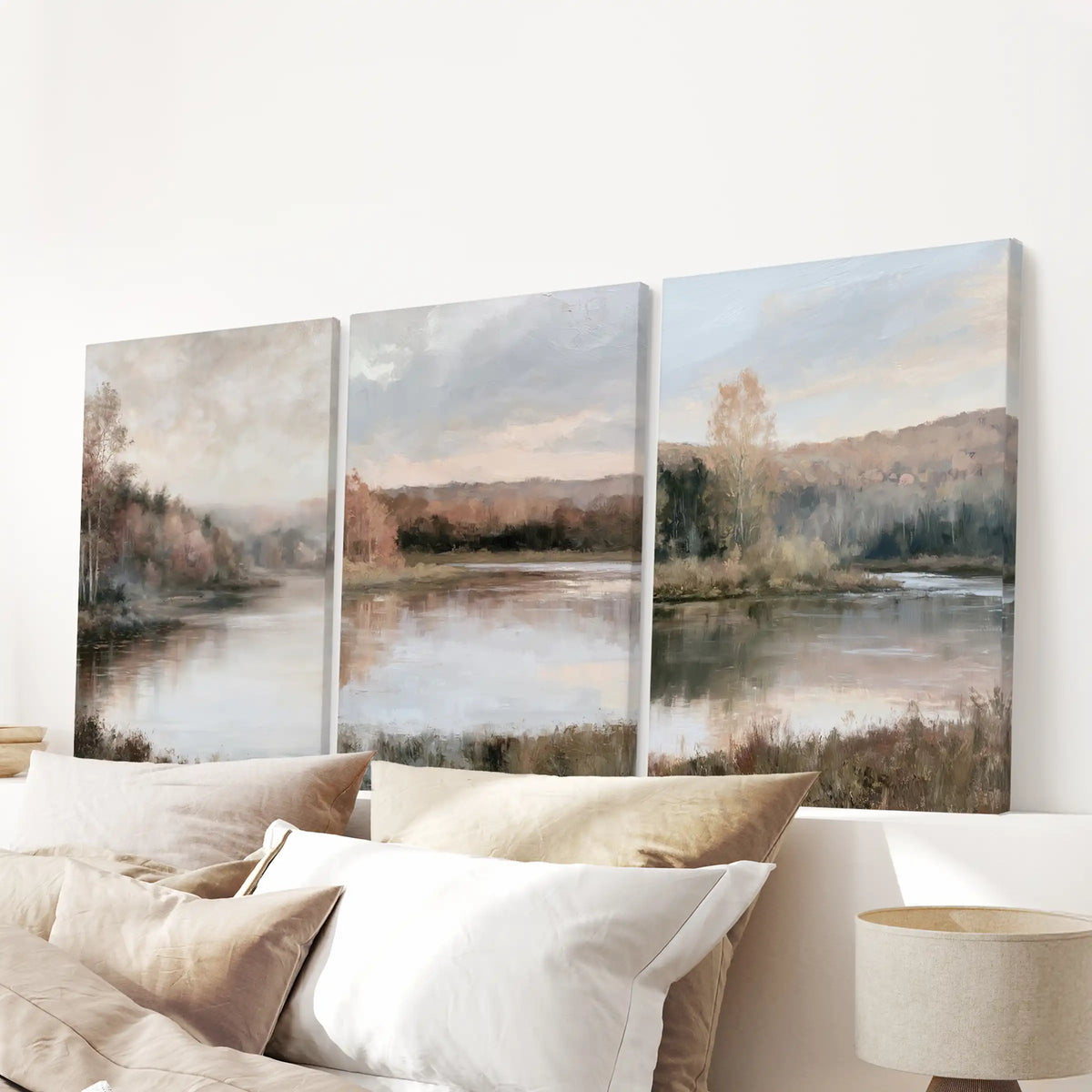 Muted shoreline and trees span the bedroom wall over the headboard as a three-piece canvas set, soft edges giving a calm, cloudlike finish without frames.