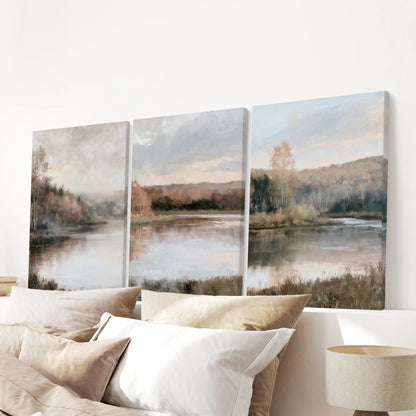 Muted shoreline and trees span the bedroom wall over the headboard as a three-piece canvas set, soft edges giving a calm, cloudlike finish without frames.