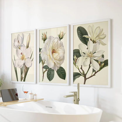 White flower studies hang in three white frames above a freestanding bathtub.
