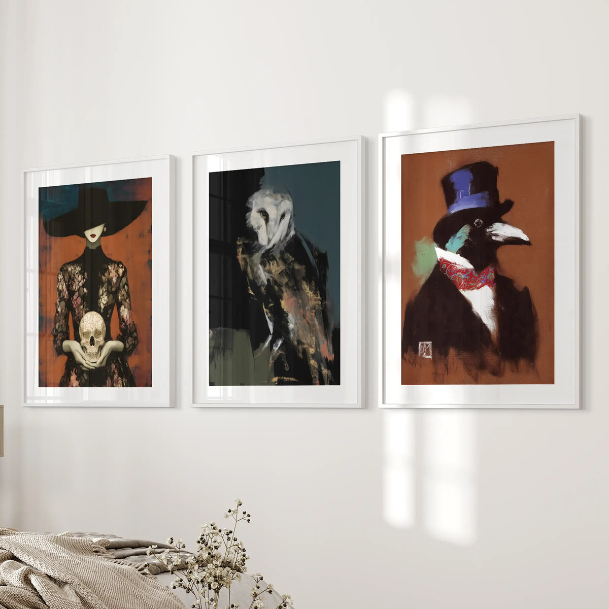 Dark academia set of three wall prints in white frames with mats, arranged on a bedside wall in a bedroom with macabre owl, skull and raven imagery.
