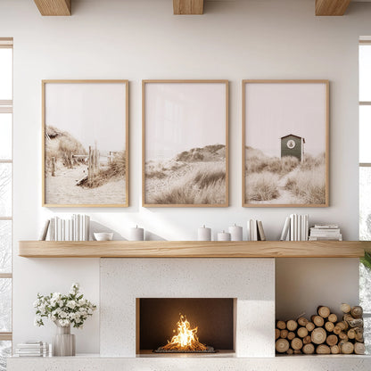 Three wood-framed wall prints of dried coastal grass rest above the fireplace, introducing organic texture and relaxed neutral calm.