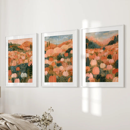 Three framed art prints depicting a pumpkin field landscape in warm autumn tones, displayed side-by-side on a white wall above a bed with neutral bedding.