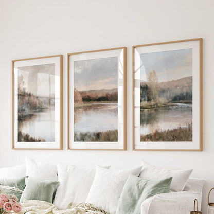 Autumn lake landscapes matted in light oak frames stretch over the sitting room sectional, a three-piece wall art arrangement with soft, cozy fall color.