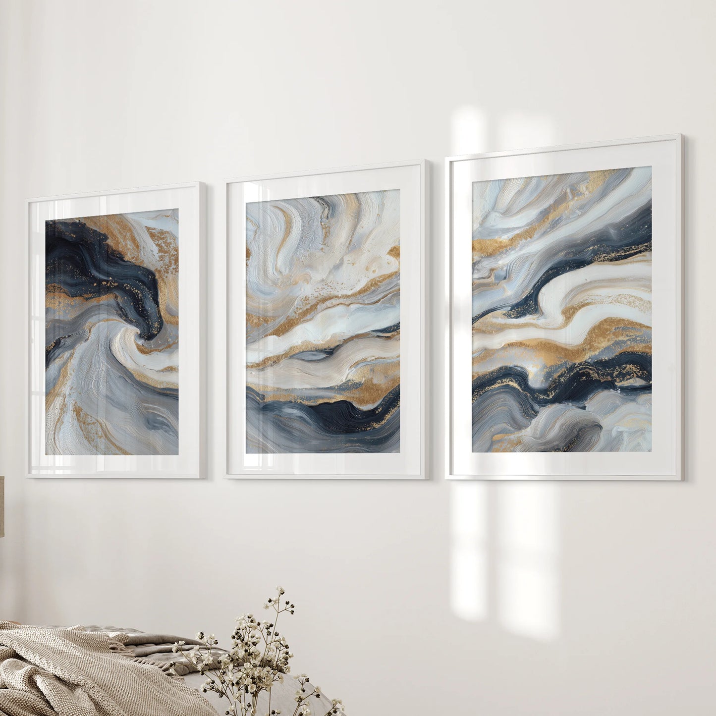 Blue and beige fluid swirls with gold, a gallery of three art prints, are white framed with mats and styled on the bedroom wall beside the bed.