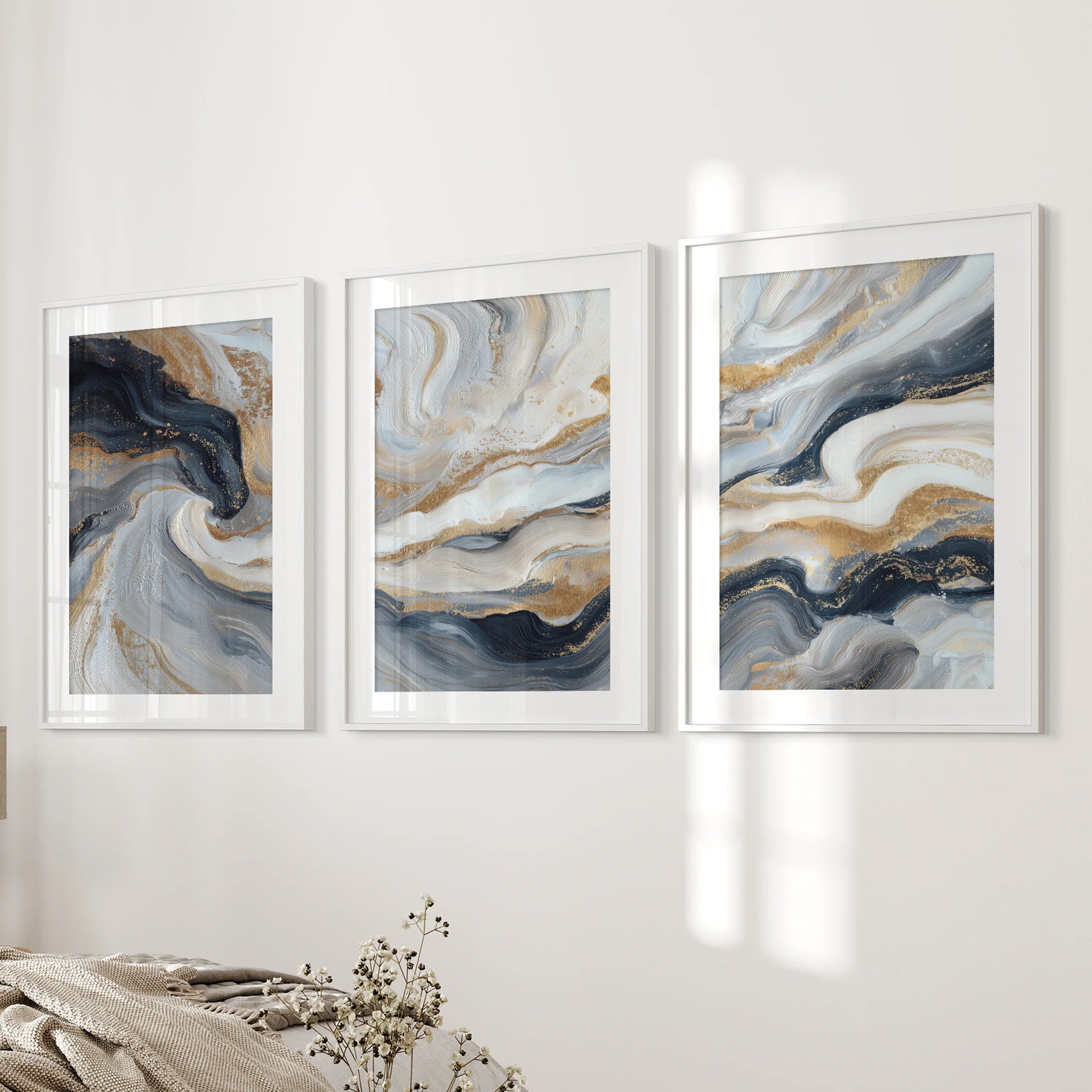 Blue and beige fluid swirls with gold, a gallery of three art prints, are white framed with mats and styled on the bedroom wall beside the bed.
