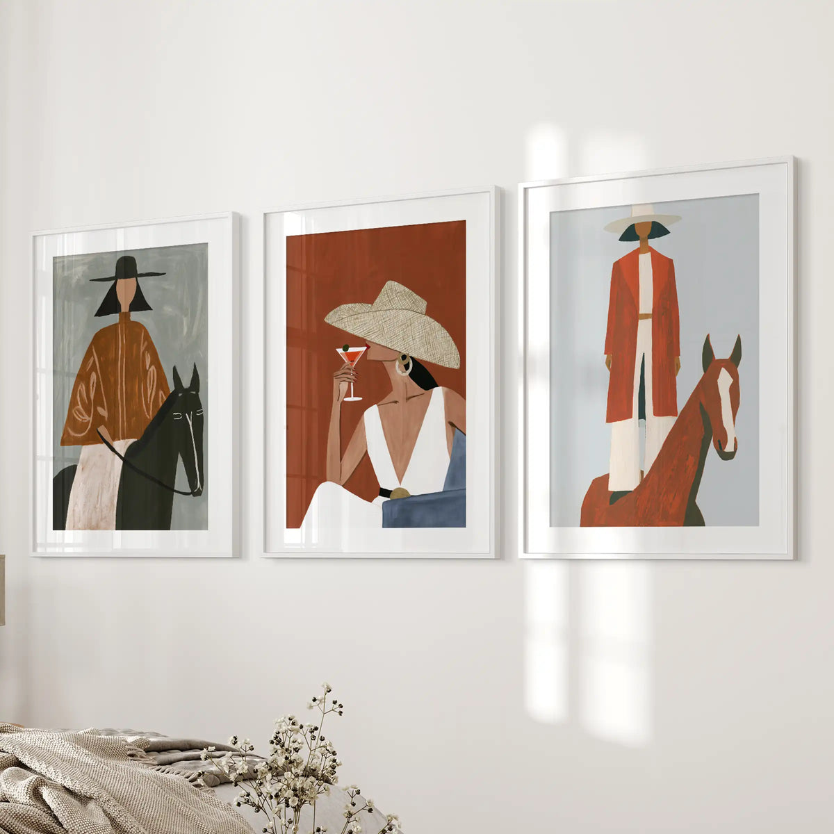 Three wall posters of western women with horses, framed in white with mats, bring softly styled art to the bedroom wall near the bed.