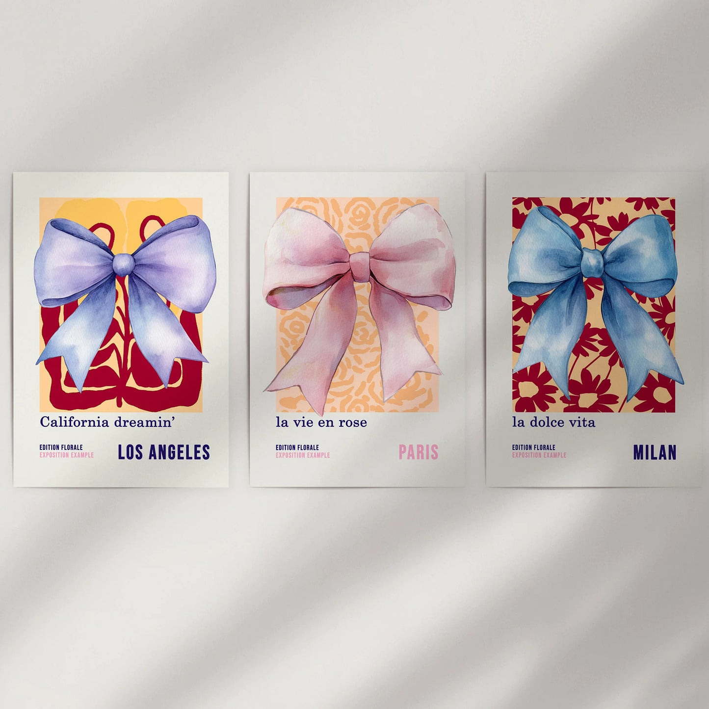 A three-piece unframed set of 70s-inspired bow posters rests on a white wall, their airy watercolors mixing retro curves with soft color.