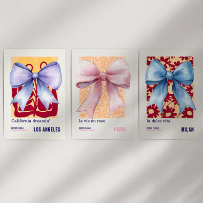 A three-piece unframed set of 70s-inspired bow posters rests on a white wall, their airy watercolors mixing retro curves with soft color.