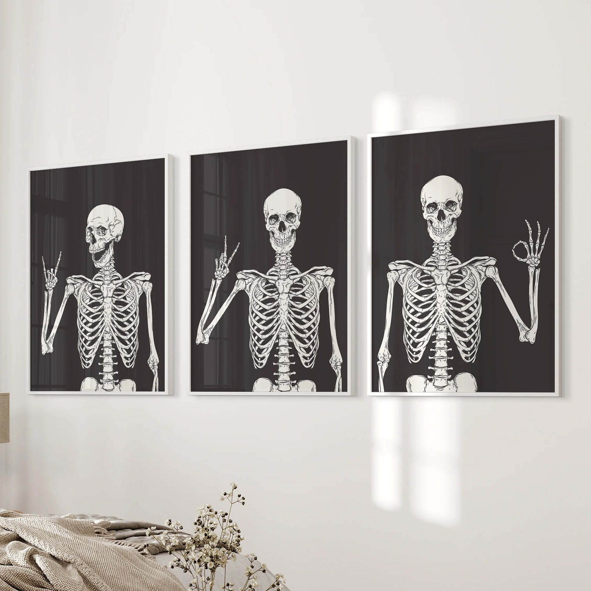 White-framed prints of a skeleton trio align as an art set of three beside the bed, brightening the bedroom with festive Halloween energy.