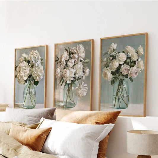 Set of three floral still life wall posters in thin wood frames, displayed over a bedroom headboard.