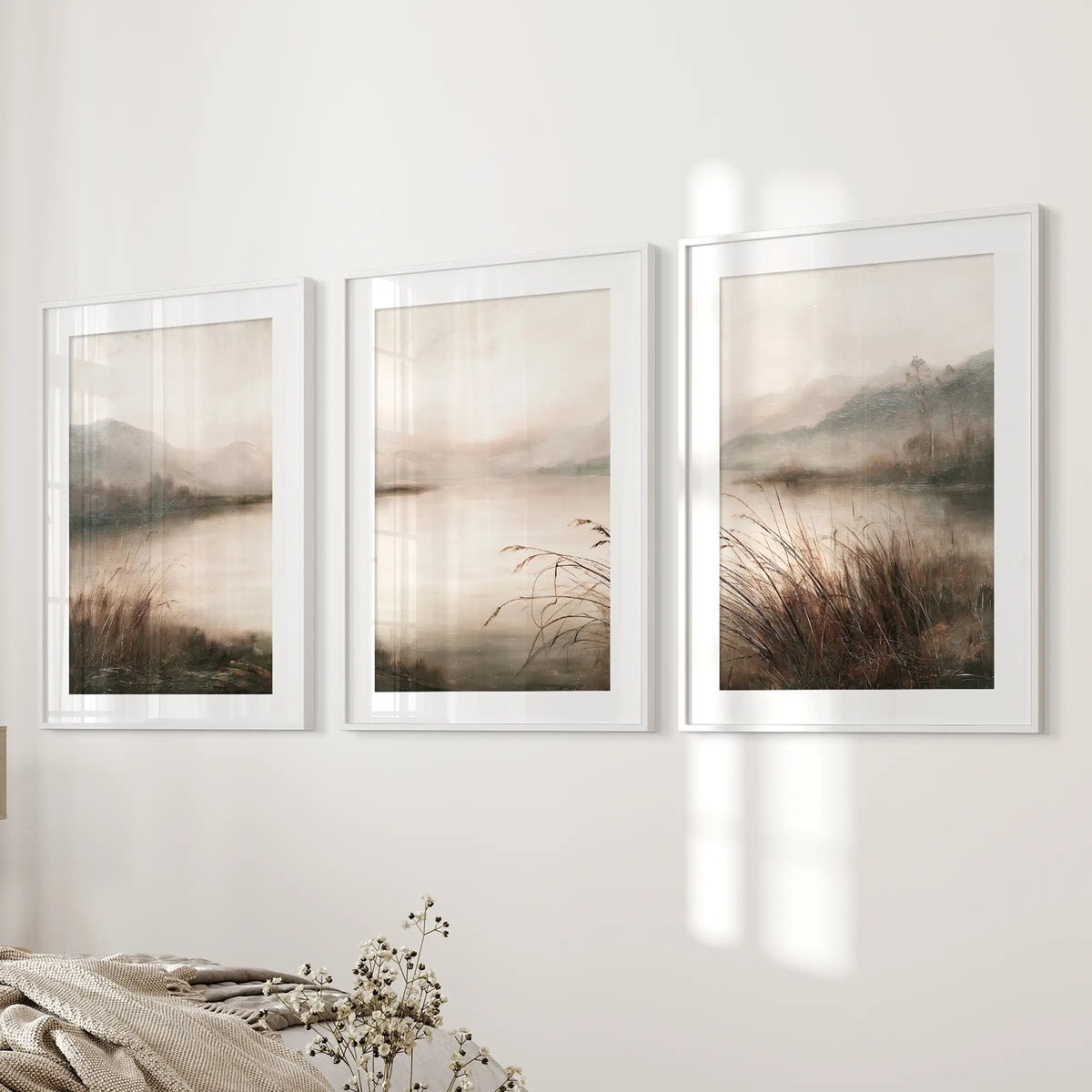 Three-piece foggy woodland lake wall art set in white matted frames, displayed beside a bed in a bedroom.