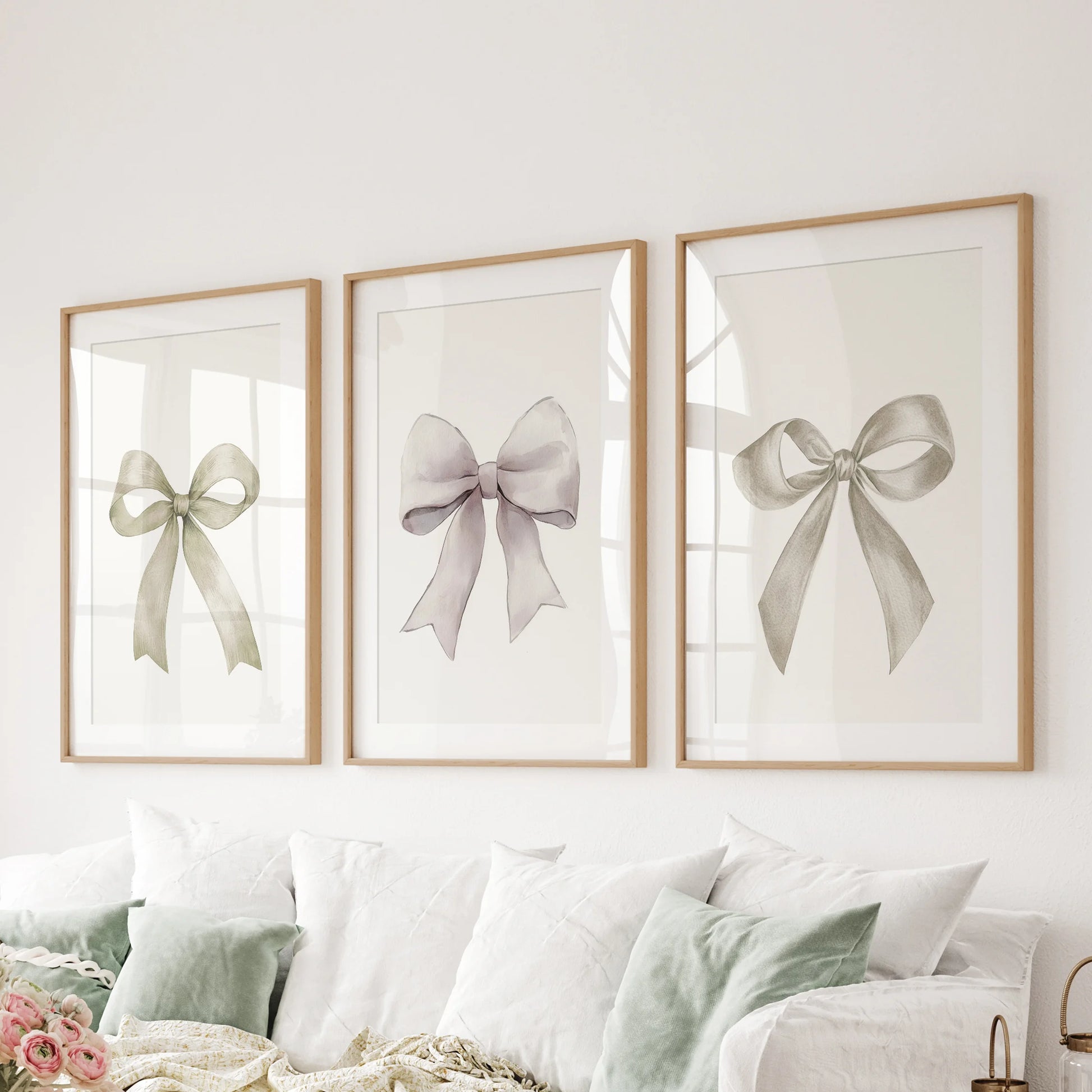 Bow motif wall art, in three pieces, layers matte light-wood frames behind the lounge couch, showcasing delicate ribbon drawings with an airy, polished feel.