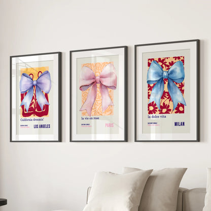 Preppy coquette bows, three-piece art prints with black mats and frames, anchor the lounge above the couch with soft blue-and-pink watercolor flair.