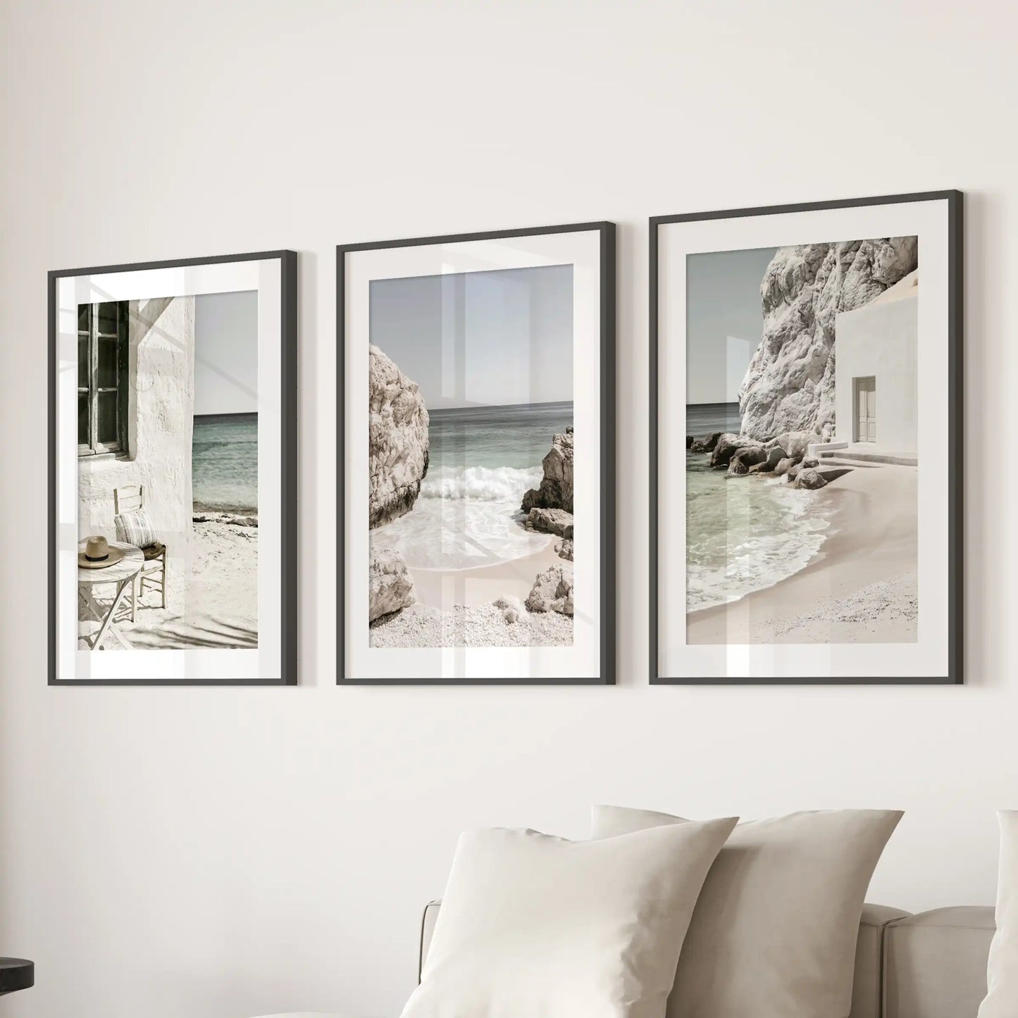 This set of three art prints shows Greek seaside beaches in black frames with white mats, styled behind the couch as a breezy living room focal point.