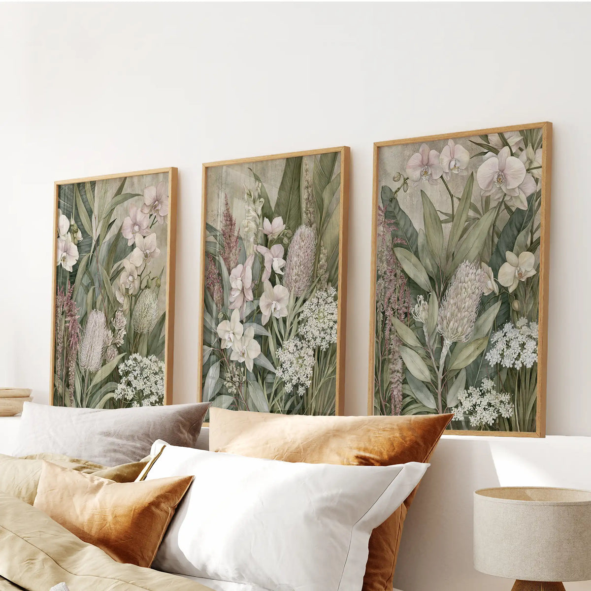 Pale orchid petals sit beside tall pink flower spikes in three oak-framed prints above a bed, with small white blooms among the green leaves.