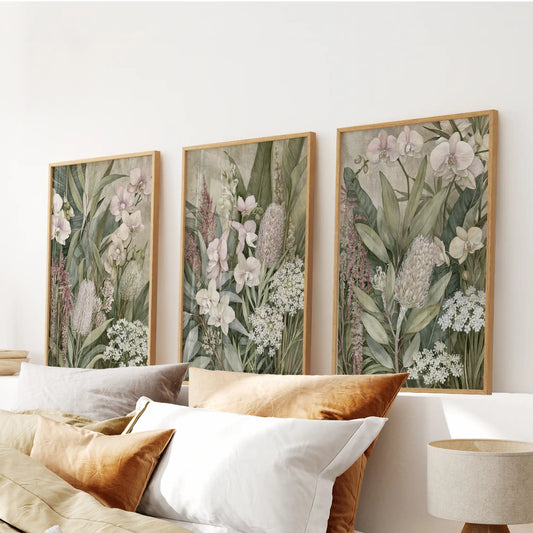 Pale orchid petals sit beside tall pink flower spikes in three oak-framed prints above a bed, with small white blooms among the green leaves.