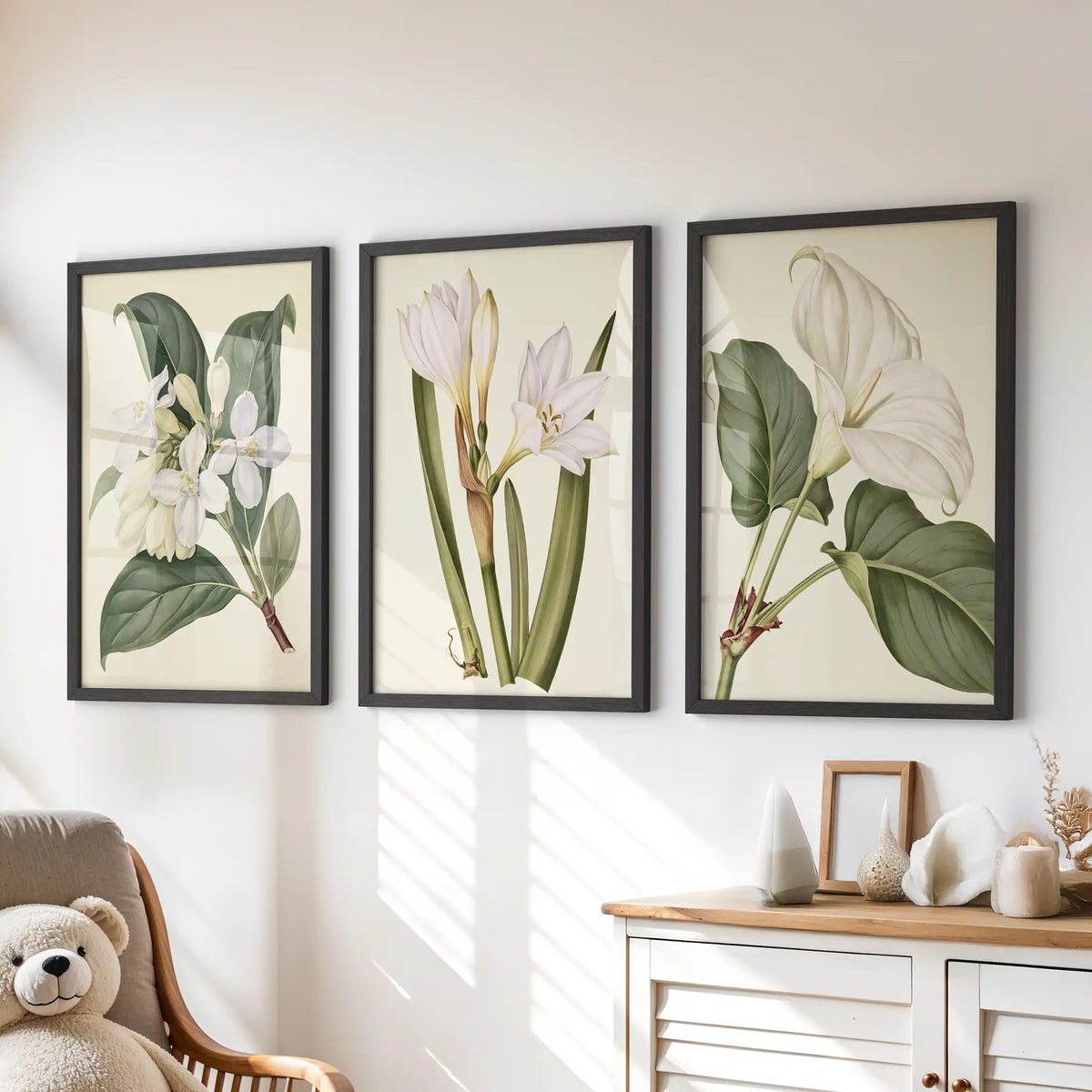 The three black frames above a dresser contain white flower studies on cream, with dense leaves at left and taller narrow stems in the middle.