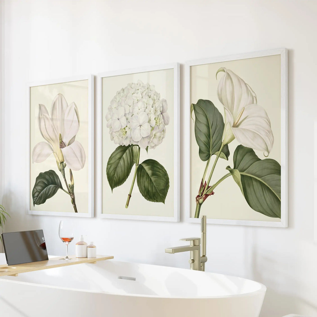 White frames surround three botanical prints above a bathtub, with a central hydrangea head and larger white blossoms on either side.