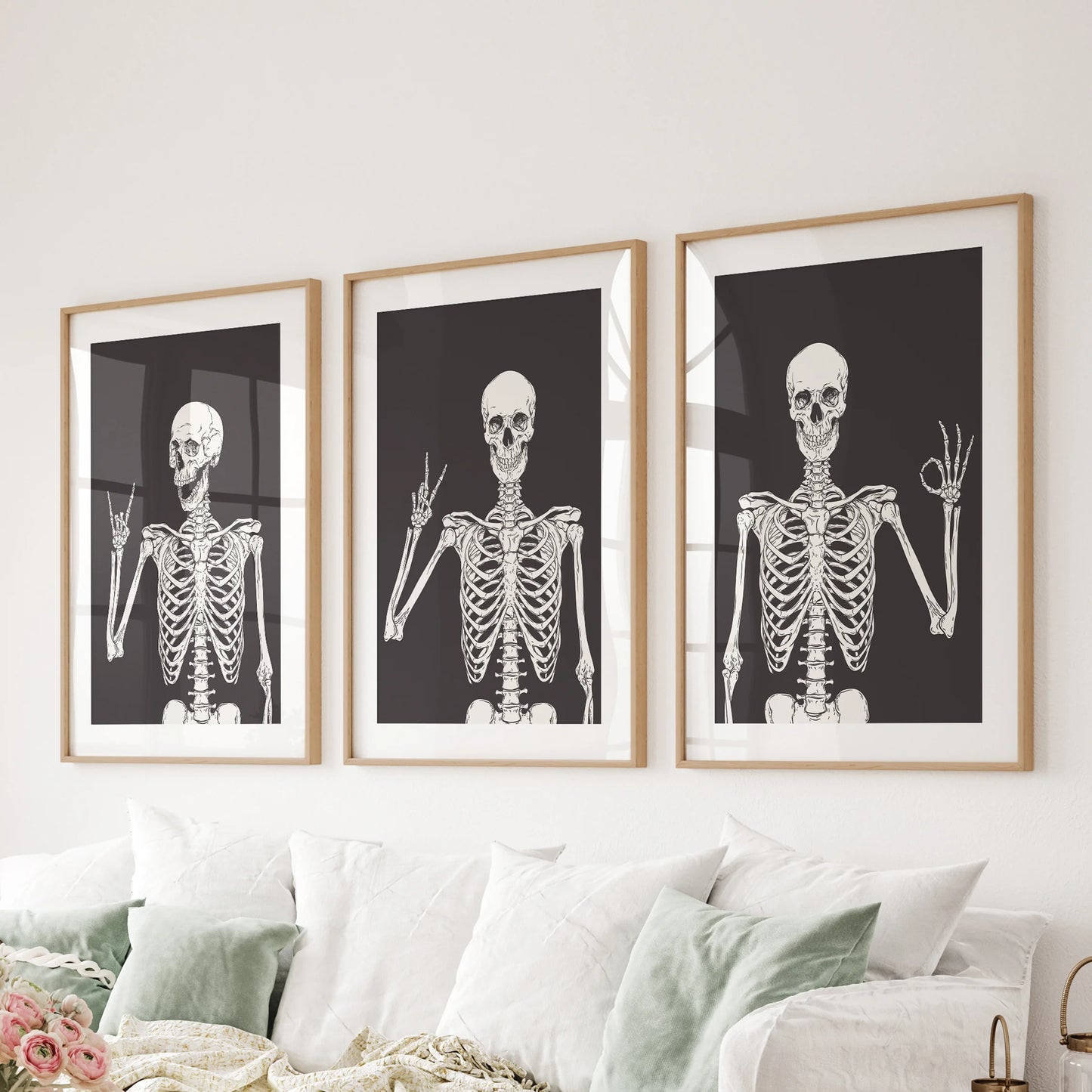 A humorous skeleton art set of three in natural oak frames with mats centers the family room wall above the sofa, soft but playful.