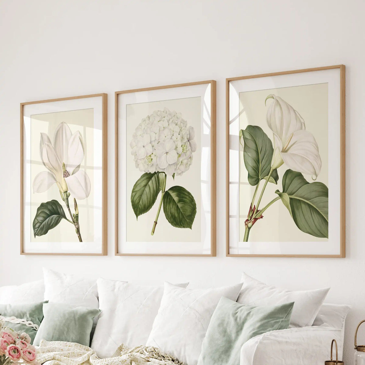 Above a sofa, matted oak frames display three white floral prints.