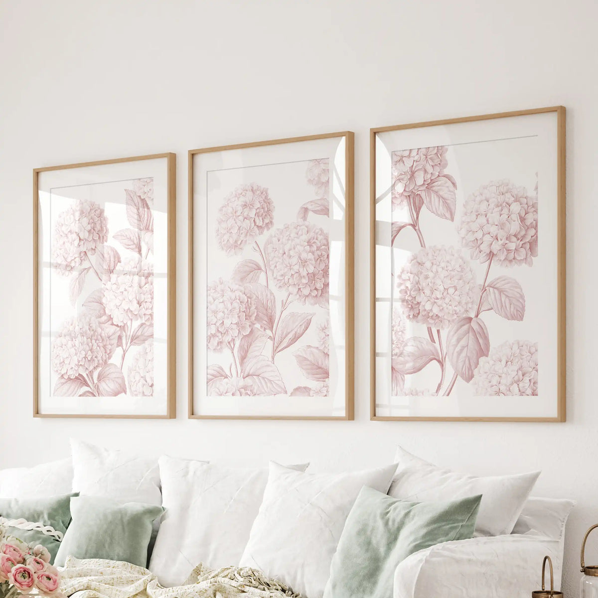 The three oak frames above a sofa have white mats around pale pink hydrangea patterns, with detailed leaf veins and petal outlines.