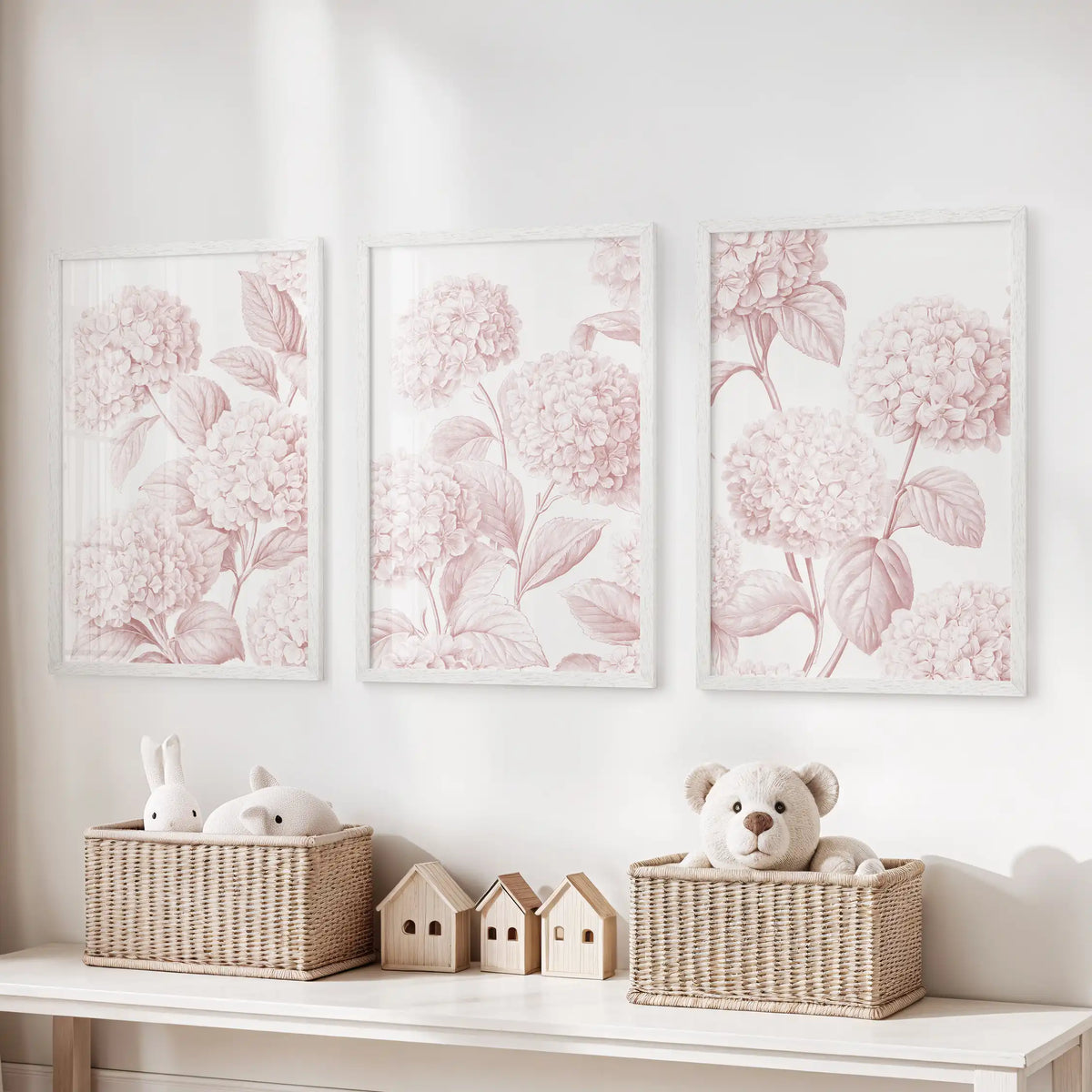 White frames hold three pink hydrangea prints above a toy storage bench.