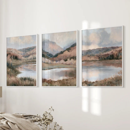 Three wall art prints of soft autumn nature scenes in slim white frames are mounted beside the bedroom bed for a gentle, neutral accent.