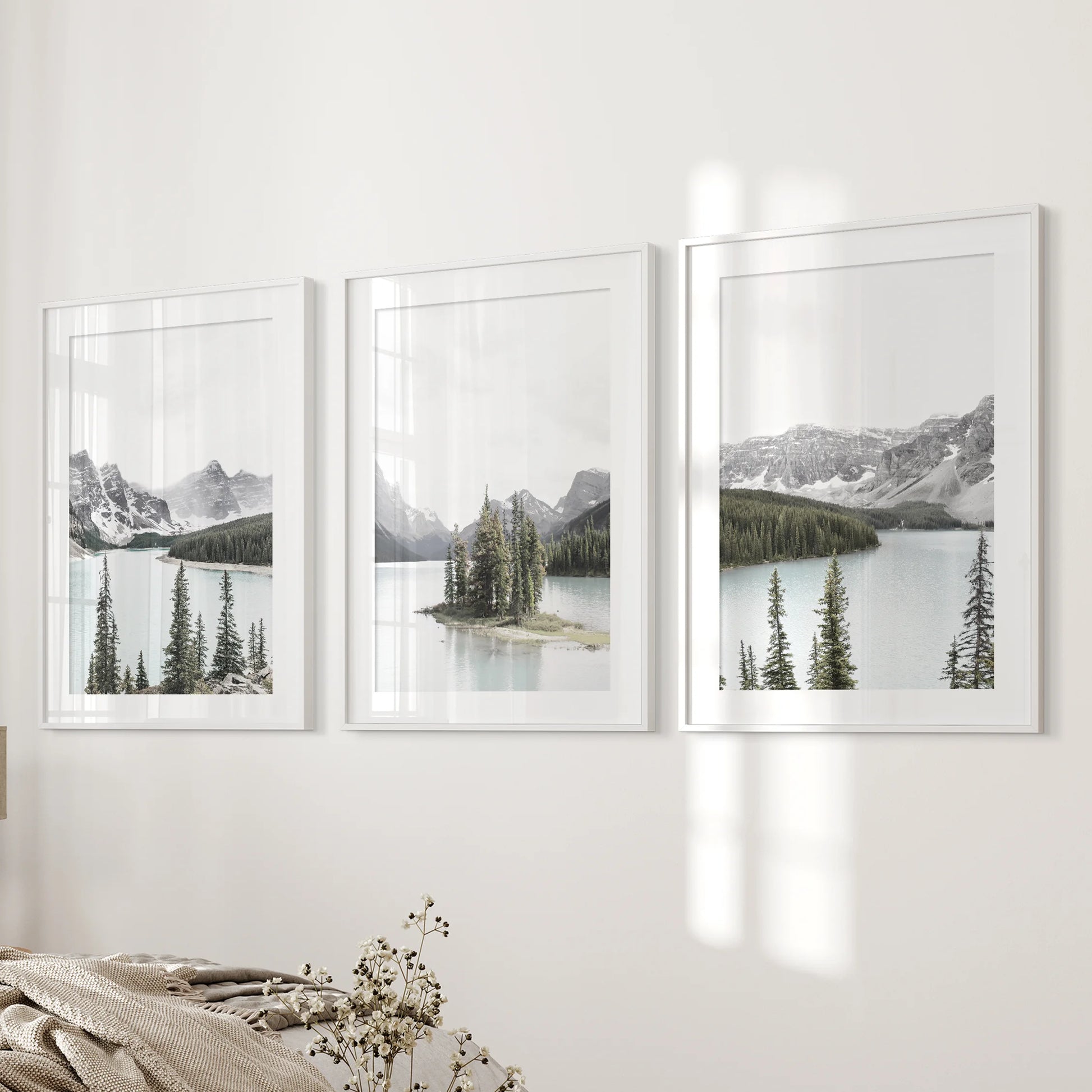 Three softly matted wall prints of an alpine lake in white frames rest beside the bed, creating a soothing focal point in the bedroom.