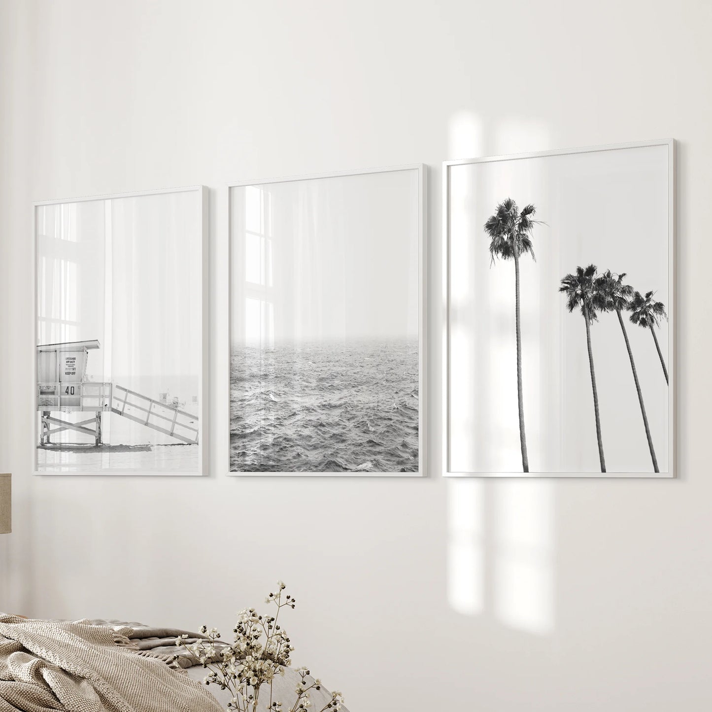 A wall art trio of lifeguard tower prints in white frames rests beside the bed, giving the bedroom a crisp coastal rhythm.