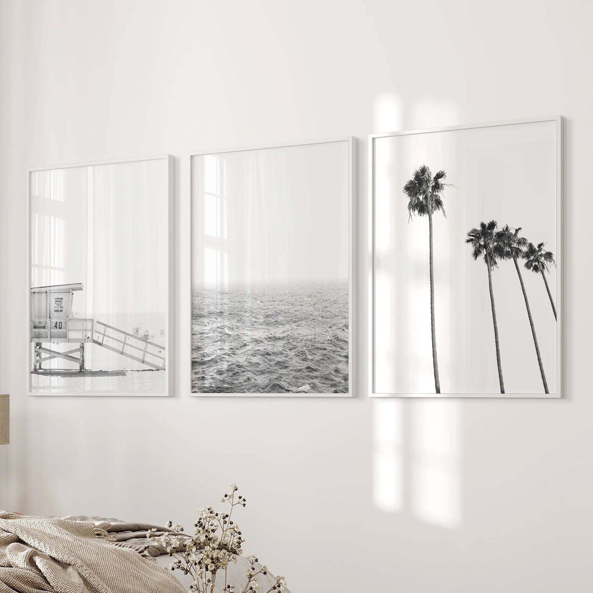 A wall art trio of lifeguard tower prints in white frames rests beside the bed, giving the bedroom a crisp coastal rhythm.