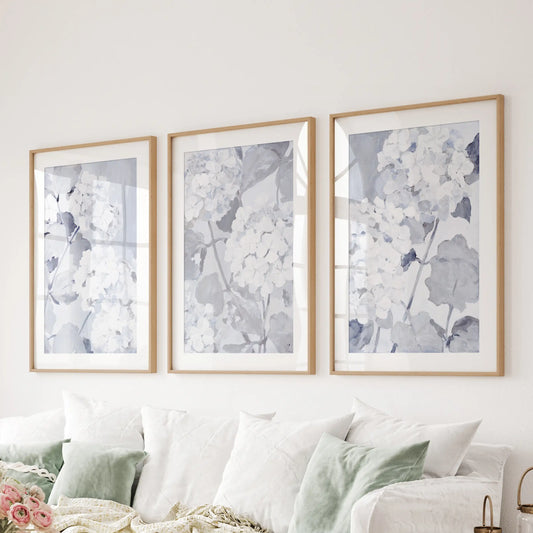 Three-piece wall art set of light blue botanicals in matted wood frames over a living room sectional.