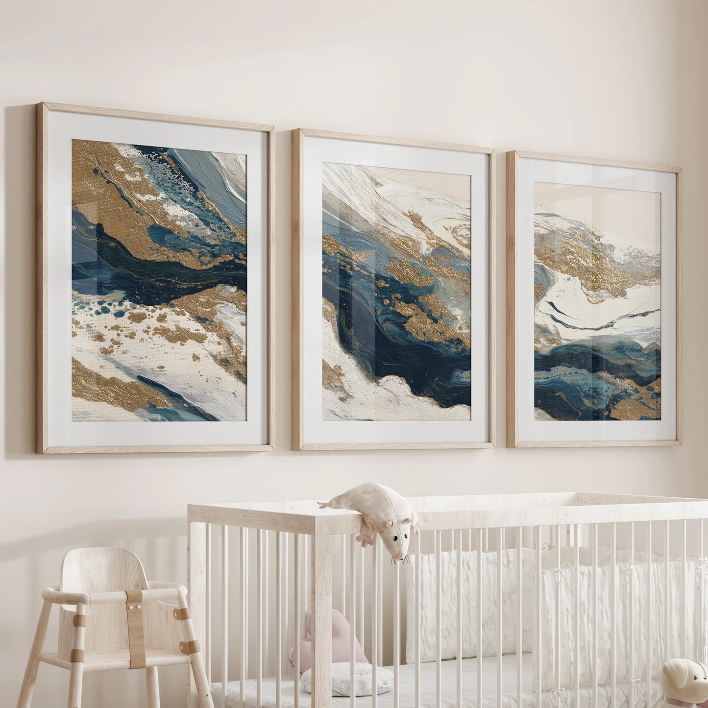 Navy blue and gold abstract brushstrokes, a gallery set of three, float above the cot in the infant room with natural oak frames and soft white mats.