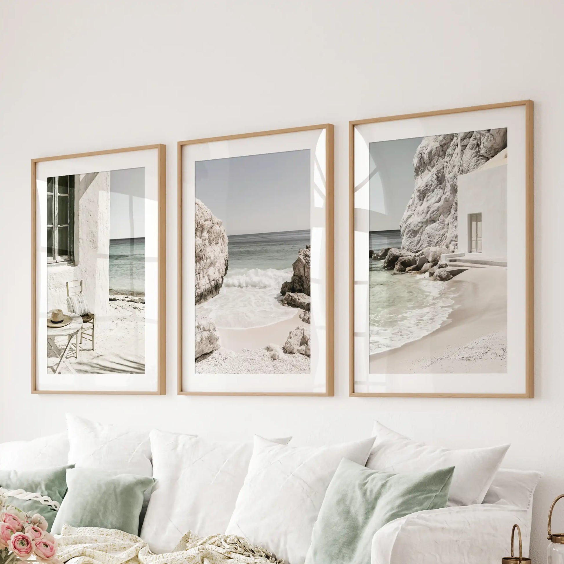 A three-piece artwork set features Mediterranean coastline vistas in natural wood frames with mats, styled behind the sofa to warm the living room with coastal light.