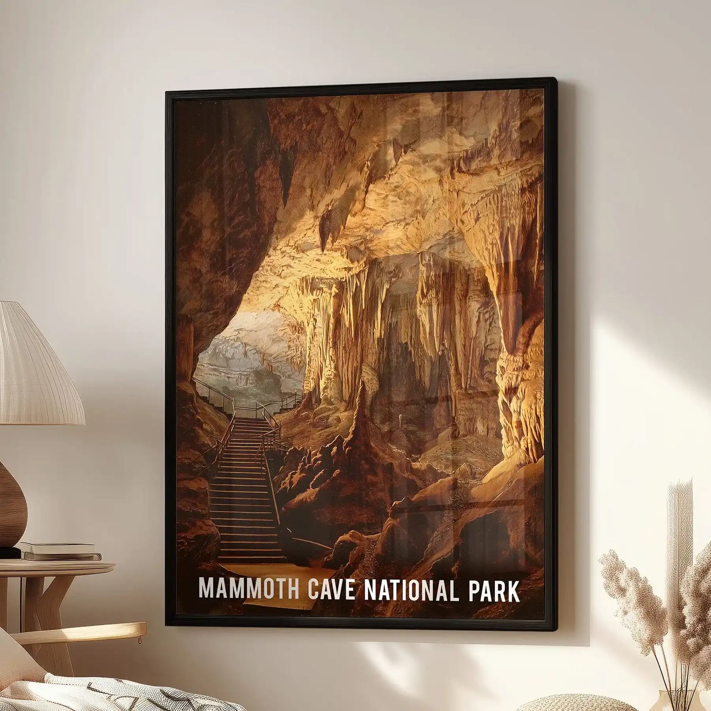 A framed wall print of Mammoth Cave National Park hangs above a cozy lounge chair, its black frame outlining a wide, amber cavern glow.