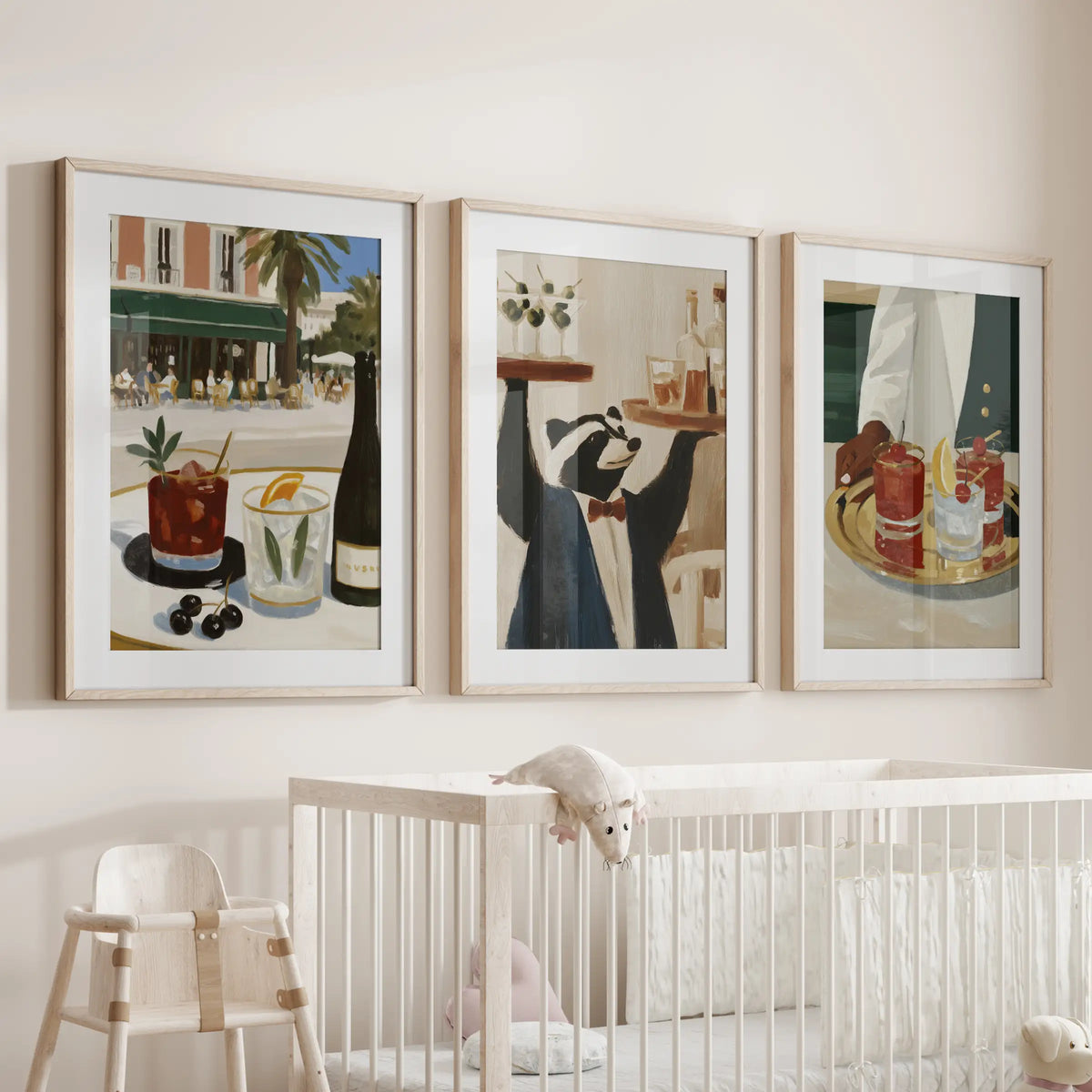 Three-print wall art set featuring martini artwork, displayed in light oak matted frames above a cot in an infant room.