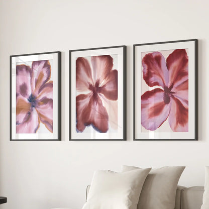 Above a sofa, three mauve petal close-up prints hang in black frames with white mats.