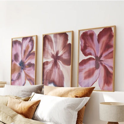 Above a bed, oak frames surround three prints of broad burgundy petals with mauve highlights.