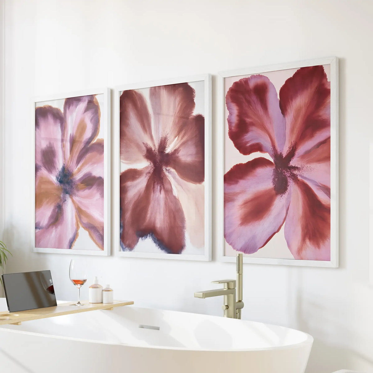 Above a freestanding bathtub, three white frames display mauve and burgundy flower prints.