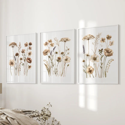 Three prints of slender meadow stems with beige and brown flowers hang beside a bed in white frames.
