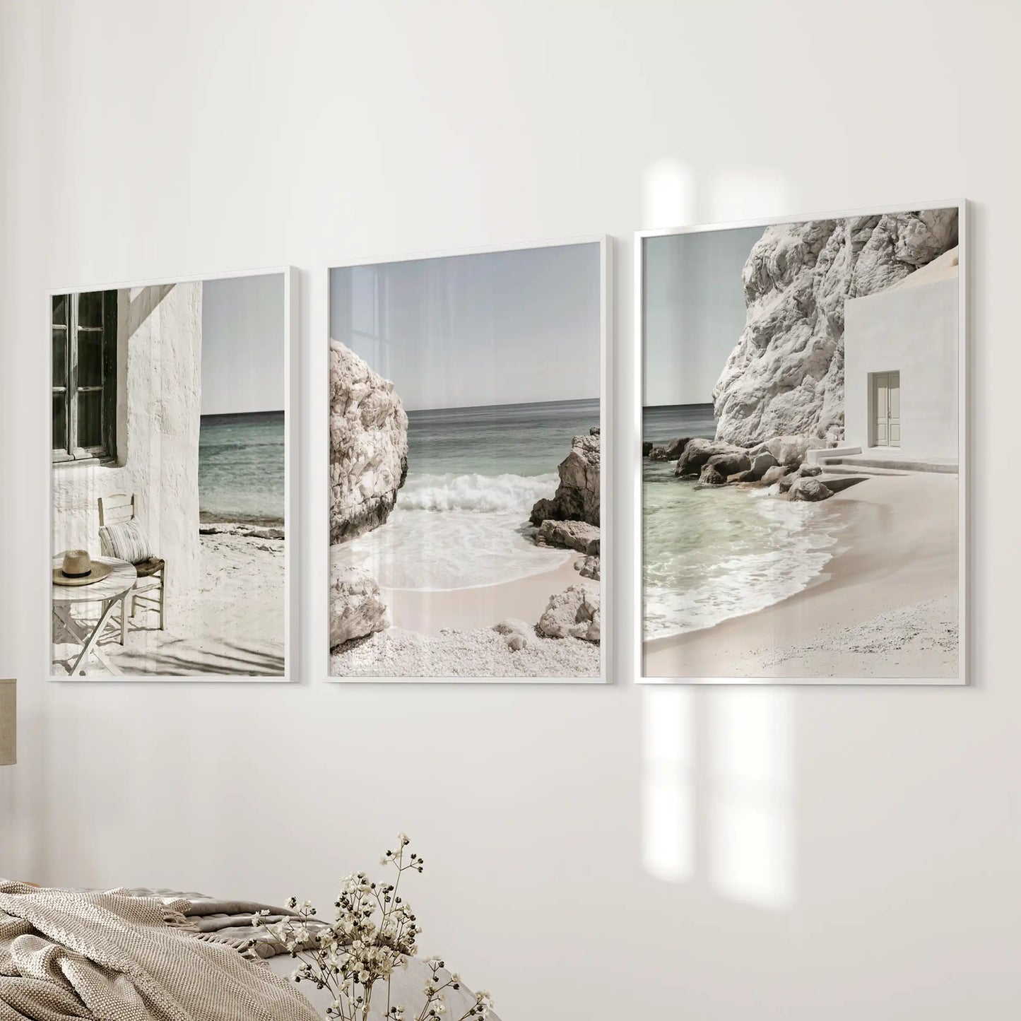 A three-piece art set showcases Mediterranean coastline vistas in crisp white frames, centered on a bedside wall for a quietly coastal bedroom mood.