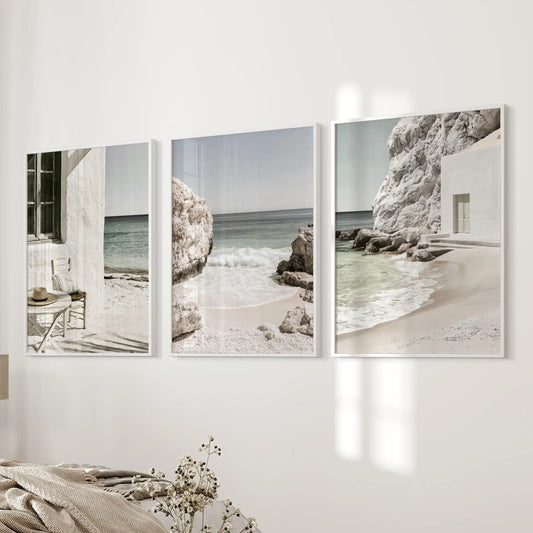 A three-piece art set showcases Mediterranean coastline vistas in crisp white frames, centered on a bedside wall for a quietly coastal bedroom mood.