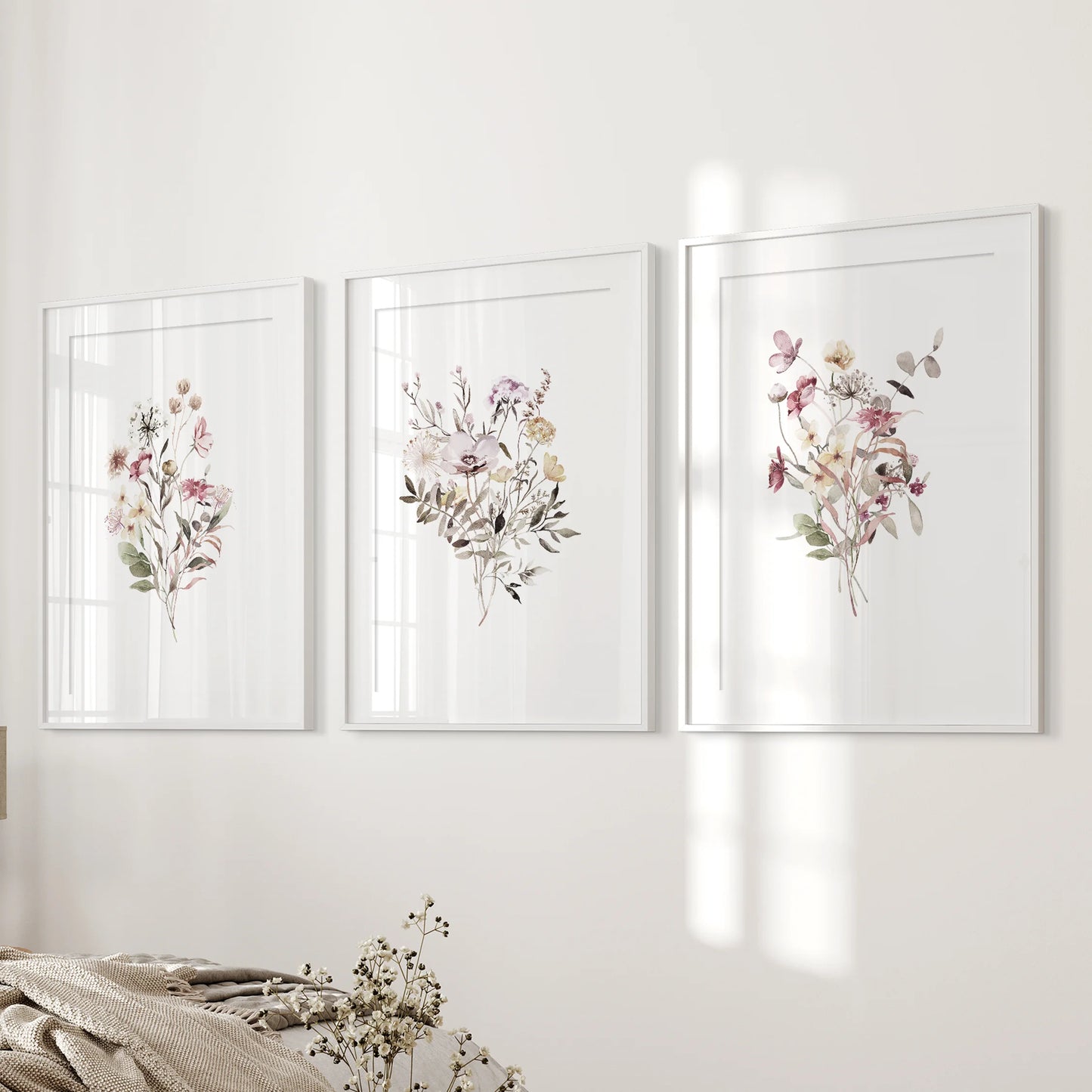 A minimal 3-piece wall hanging of matted flower prints in white frames stands next to the bed, giving the bedroom a tidy, gentle feel.