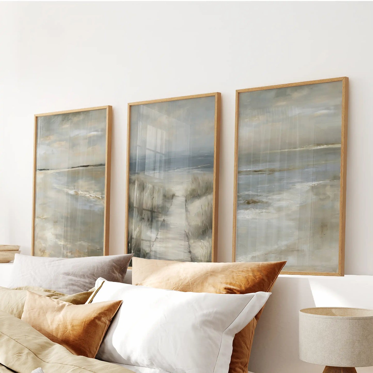 Light-wood framed wall art showing soft sand textures, a 3-panel set, rests above the bed headboard for an airy coastal atmosphere.