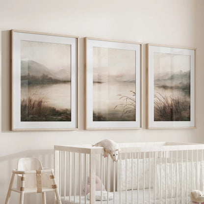 Three-piece misty lake landscape wall art set in matted oak frames, displayed above a crib in a nursery.
